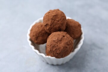 Delicious homemade candies powdered with cocoa in bowl on light table, closeup