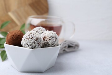Delicious homemade candies with cocoa powder and coconut flakes in bowl on white table, closeup. Space for text