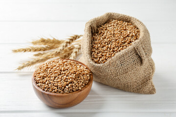 Wheat grains in bowl, burlap bag and spikelets on white wooden table, closeup