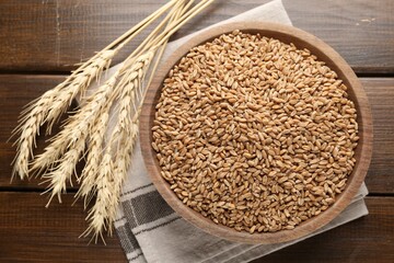 Wheat grains in bowl and spikelets on wooden table, flat lay