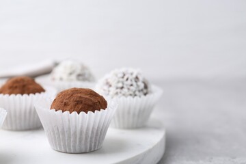 Delicious homemade candies with cocoa powder and coconut flakes on light grey table, closeup. Space for text