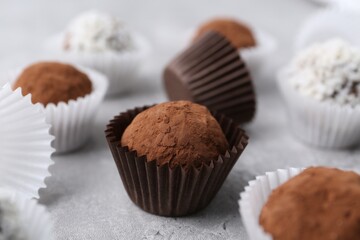 Delicious homemade candies with cocoa powder and coconut flakes on light grey table, closeup