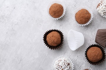 Delicious homemade candies with cocoa powder and coconut flakes on light grey table, flat lay. Space for text