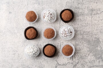 Delicious homemade candies with cocoa powder and coconut flakes on light grey table, flat lay