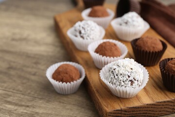 Delicious homemade candies with cocoa powder and coconut flakes on wooden table, closeup. Space for text