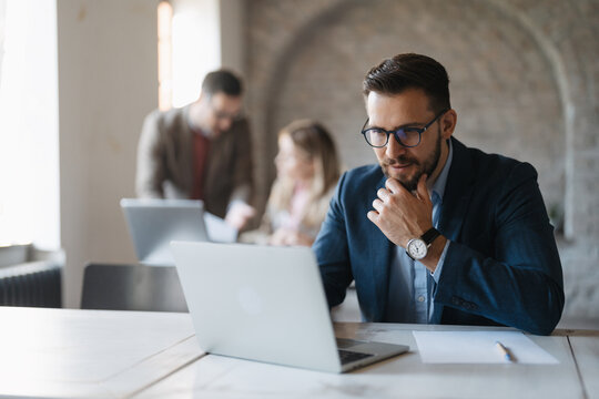 Young professional with glasses using laptop, thoughtful expression