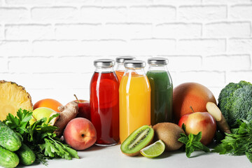 Tasty juices in glass bottles and ingredients on white table against brick wall