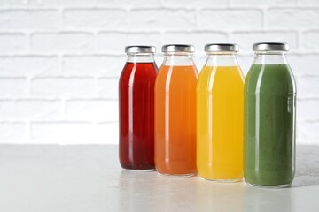 Tasty juices in glass bottles on white table against brick wall, space for text