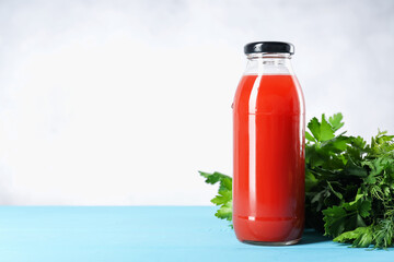 Tasty juice in glass bottle, parsley and dill on light blue wooden table, closeup. Space for text