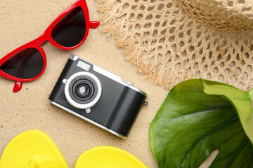 Time for summer vacation. Camera, green leaf and beach accessories on sand, flat lay