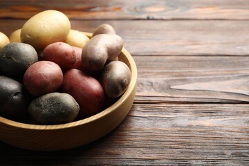 Different types of potatoes in bowl on wooden table, closeup. Space for text