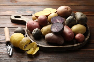 Different types of potatoes and peeler on wooden table, closeup