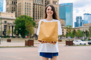 Fototapeta premium Happy woman holding kraft paper shopping bag outdoors in city