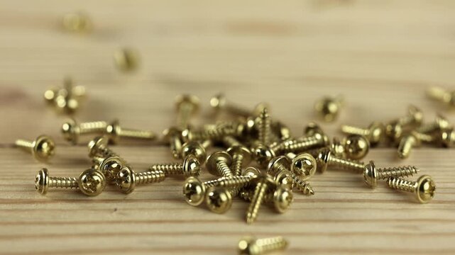 A collection of golden screws scattered on a wooden surface. The screws vary in size and shape, showcasing their metallic finish and detailed threading.