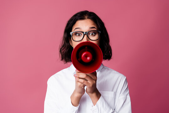 Young woman holding a red megaphone wearing a white shirt on a pink background emphasizing stylish communication - Powered by Adobe