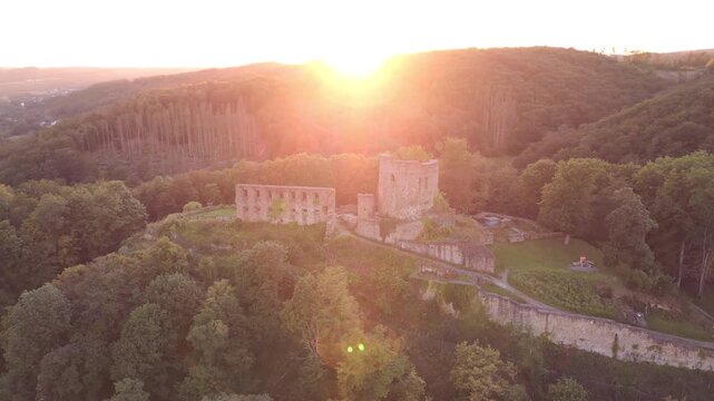 Close drone orbit around Windeck Castle ruins in North Rhine-Westphalia, Germany, with golden hour sunlight and warm backlight creating a dramatic and romantic medieval atmosphere