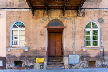 Historic townhouse in Kalisz, entrance with wooden doors and arched windows, visible facade damage and peeling plaster. Architectural heritage in need of renovation