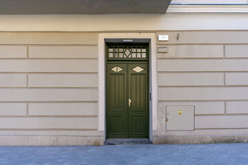 Historic townhouse in Kalisz, green wooden entrance door with glass panels, simple light-colored facade. Element of traditional urban architecture in Poland.