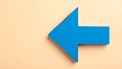 Blue wooden arrow pointing left on beige backdrop. Return, backtracking, business concept.