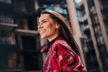 Fototapeta premium Charming young woman in vibrant red jacket smiling outdoors in urban street setting during daylight