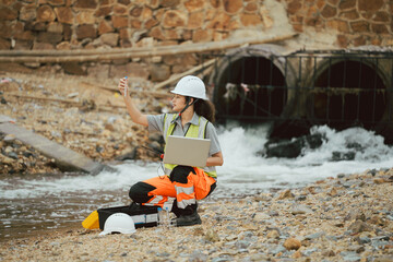 Female engineer with laptop inspecting water drainage in test tube, collecting sample for research...
