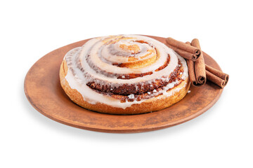 One brown delicious homemade cinnamon roll bun or swirl glazed with sweet sugar icing served on ceramic plate with spice ingredient sticks isolated on white background as freshly baked pastry dessert