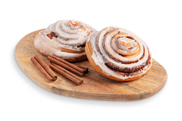 Crusty sweet freshly baked homemade cinnamon bun rolls glazed with sugar icing served with spice sticks on wooden cutting board isolated on white background as pastry dessert snack for breakfast