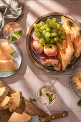 Summer party with fruit and homemade iced peach lemonade with mint in glass on pink tile background in bright morning light, top view