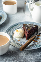 A piece of chocolate brownie cake on blue plate served with a scoop of ice cream and caramel topping with coffee
