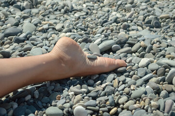 close-up - female leg on pebble beach by the sea