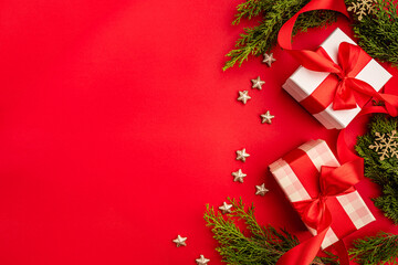 Christmas background with gift boxes with red ribbons, green pine branches, and golden stars on red surface. Perfect for holiday cards, banners, and festive ads.