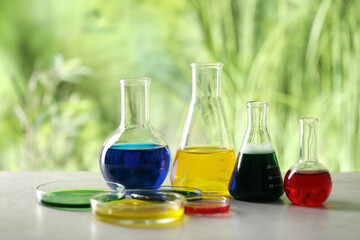 Laboratory glassware with different samples on light grey table outdoors. Solution chemistry
