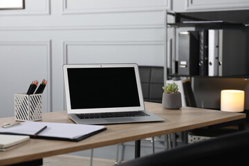 Stylish workplace with laptop, stationery and floral decor on wooden table in office