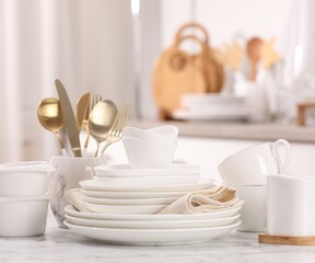 Different clean white dishware, cups and cutlery on marble table indoors