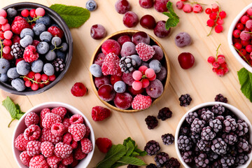 Different ripe frozen berries and mint leaves on light wooden table, flat lay