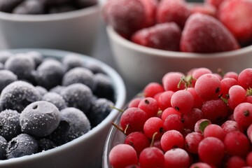 Different ripe frozen berries in bowls on table, closeup