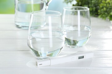 Nitrate tester and glasses of water on white wooden table, closeup