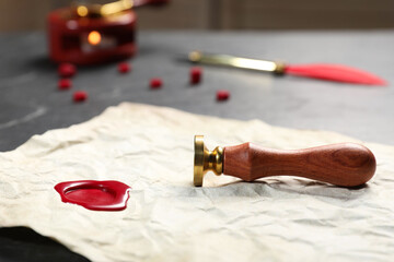 Crumpled paper with wax seal and stamp on black table, closeup