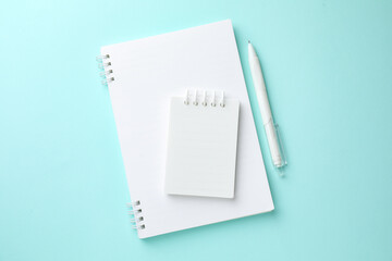 White notebooks and pen on light blue background, flat lay