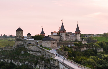 Fototapeta premium Majestic medieval Kamianets-Podilskyi fortress with towering spires and stone walls, surrounded by lush greenery and a winding path, evoking a sense of history and architectural grandeur