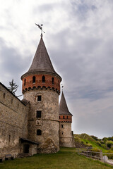 Medieval Kamianets-Podilskyi fortress with towering spires and weathered stone walls, surrounded by lush greenery, showcasing historical architecture and ancient craftsmanship in a serene landscape