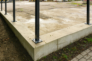 New fence construction with concrete foundation and anchored black metal posts at worksite © Zigmunds