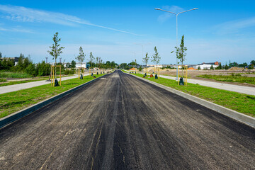 Fototapeta premium Newly paved asphalt road with sidewalks, young trees, and street lighting in modern urban development