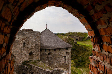Fototapeta premium Medieval Kamianets-Podilskyi fortress viewed through an archway, showcasing stone walls, grassy landscape, and a thatched roof, embodying historical architecture and cultural heritage