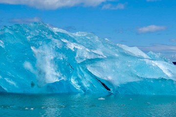 A large, translucent blue iceberg with a textured surface floating in the water.