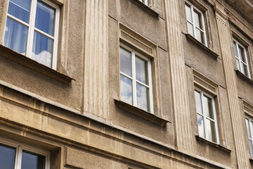 Old tenement house facade with classic architectural details and windows reflecting blue sky. Historical residential building in European city. Vintage architecture background with old textured wall.