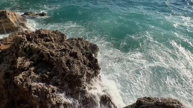 Witness the vibrant turquoise waves dramatically crashing onto stones. An awe-inspiring coastal visual ideal for travel and nature documentaries.
