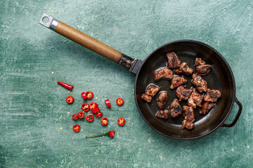 Tasty grilled meat sizzling in a cast iron skillet, placed on a vintage green wooden table. Rustic overhead shot with empty copy space for text or menu design.