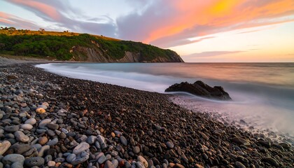 A tranquil coastal scene at sunrise, showcasing a pebble beach meeting a serene ocean under a vibrant sunrise sky.