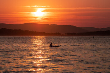Fototapeta premium Kayaker on the Adriatic Sea during sunset in Biograd na Moru, Croatia. Peaceful seascape with warm orange light and silhouette, ideal for wall art and relaxation themes.